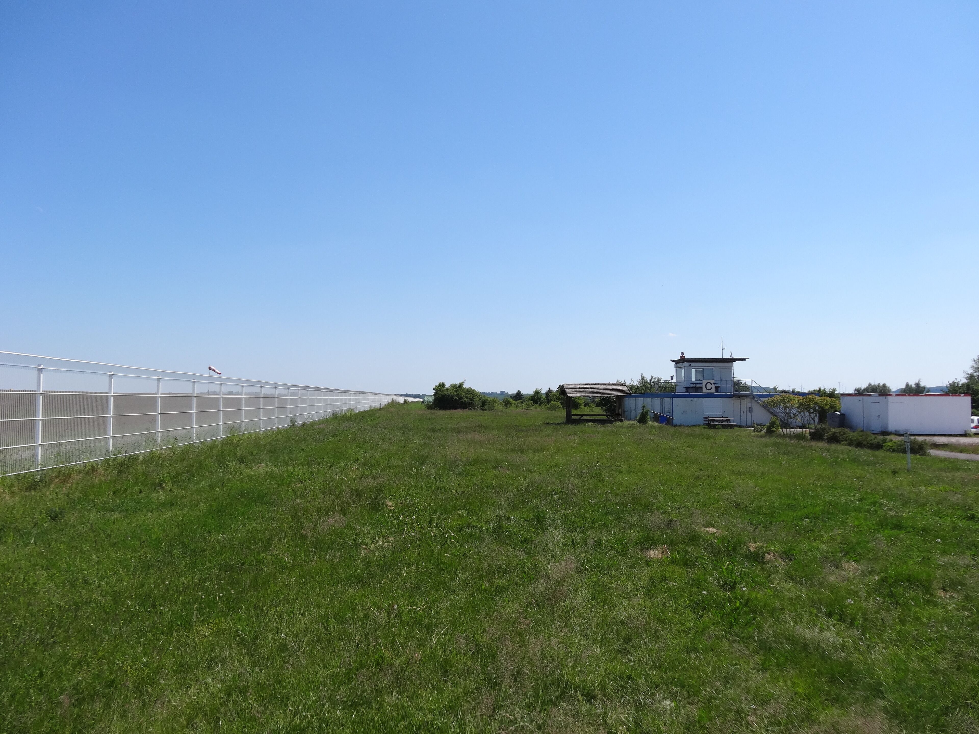 A grassy field with a greenhouse structure and a small building with a blue roof.