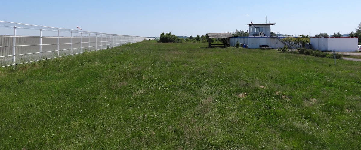 A grassy field with a greenhouse structure and a small building with a blue roof.