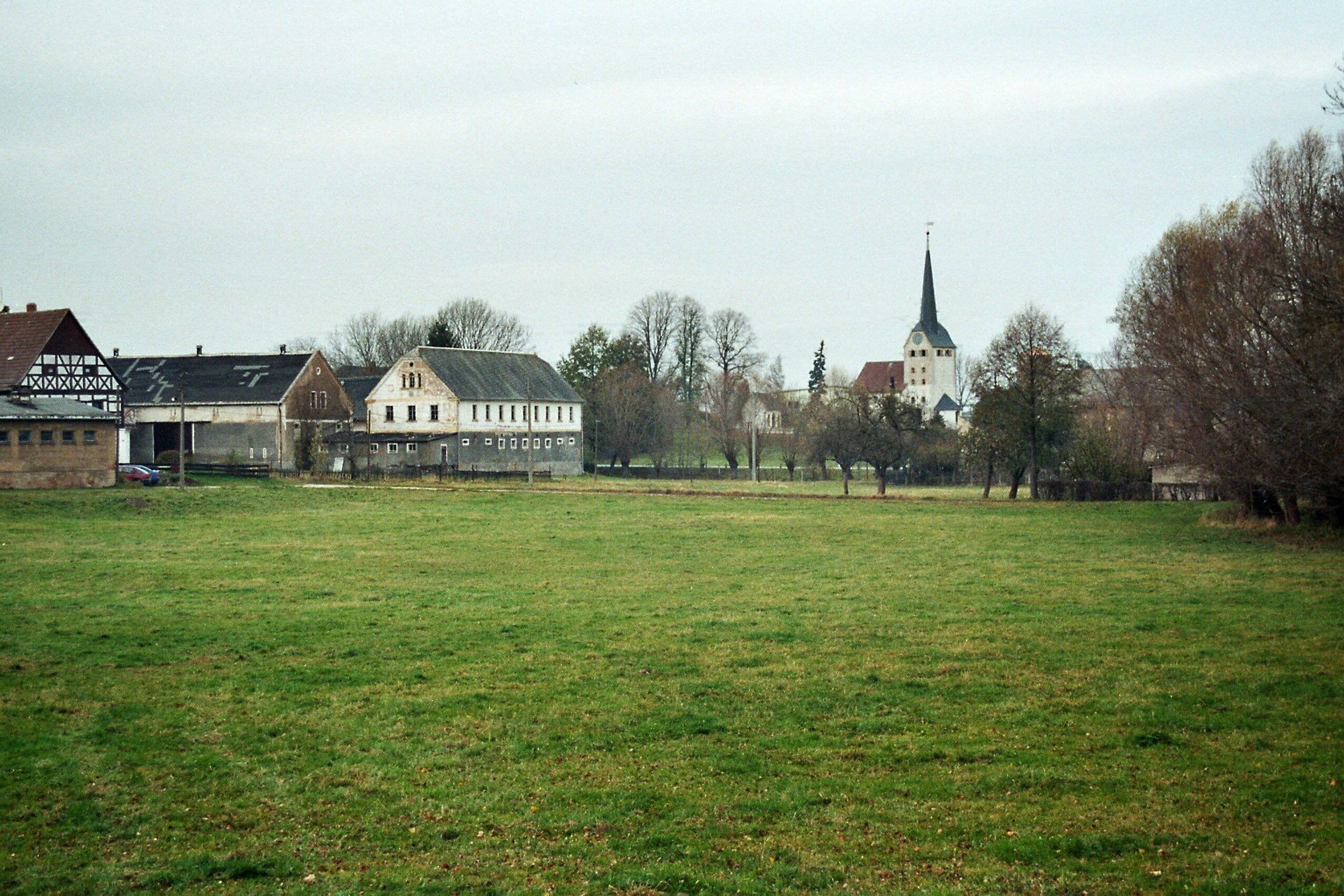 A rural landscape with a church steeple, a large barn, and a field.