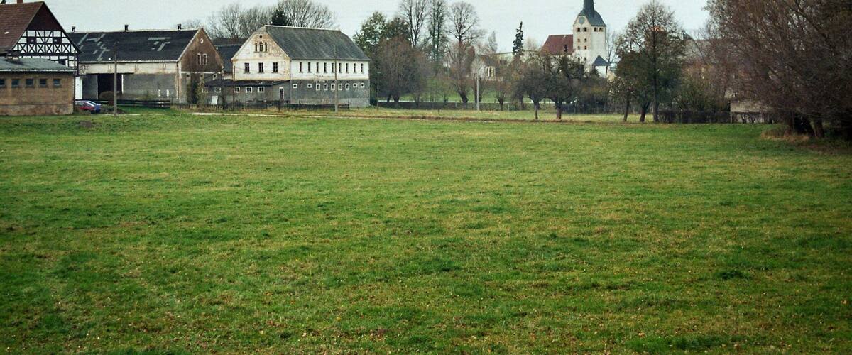 A rural landscape with a church steeple, a large barn, and a field.