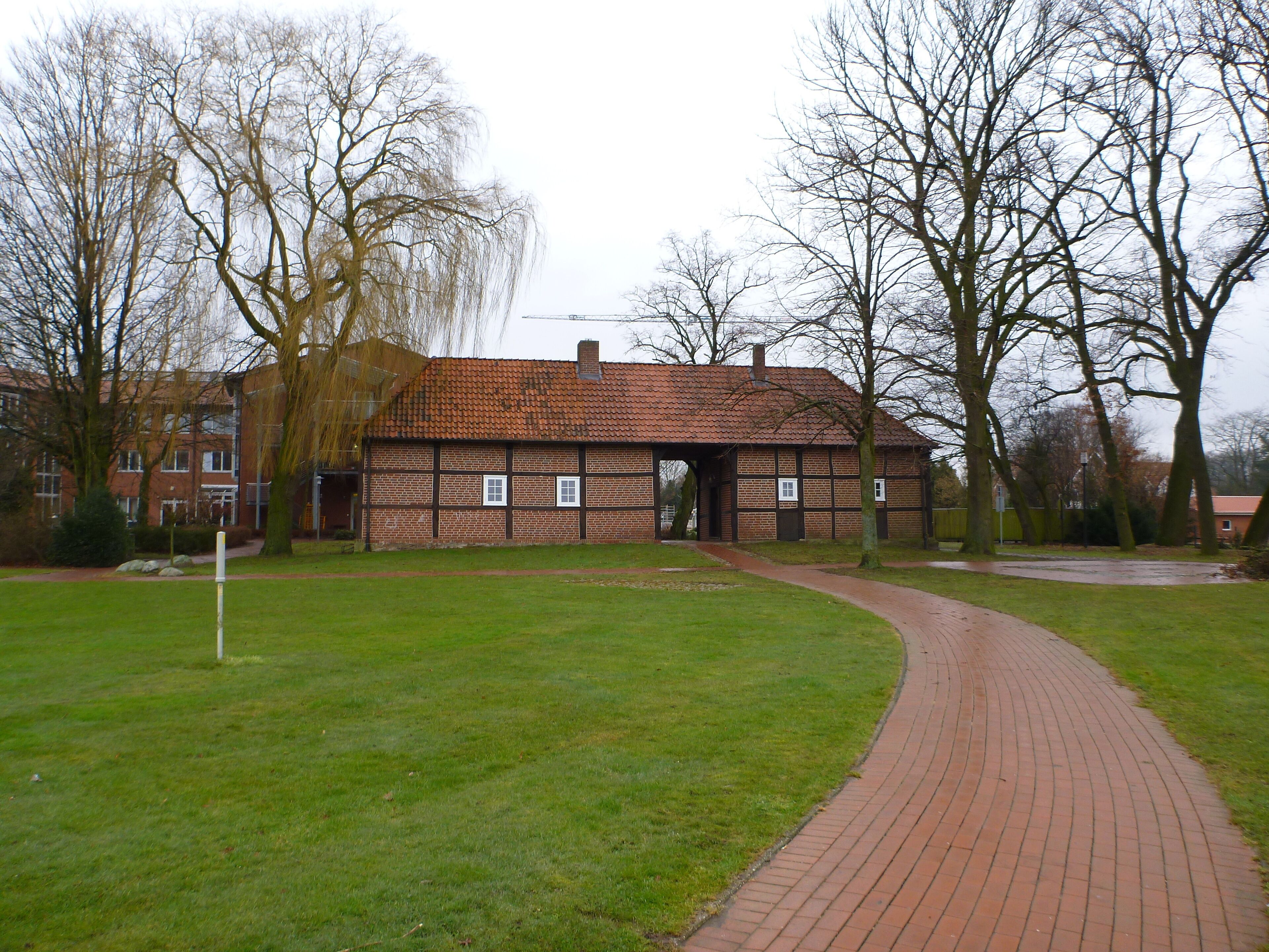 A brick building with a tiled roof, surrounded by trees and a brick pathway.
