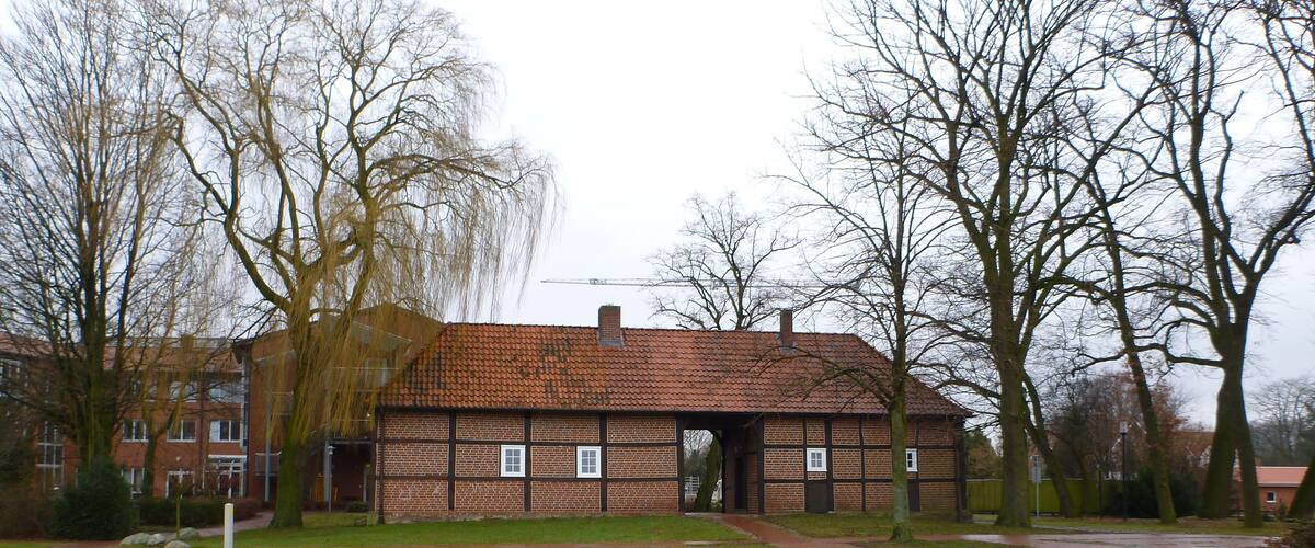 A brick building with a tiled roof, surrounded by trees and a brick pathway.