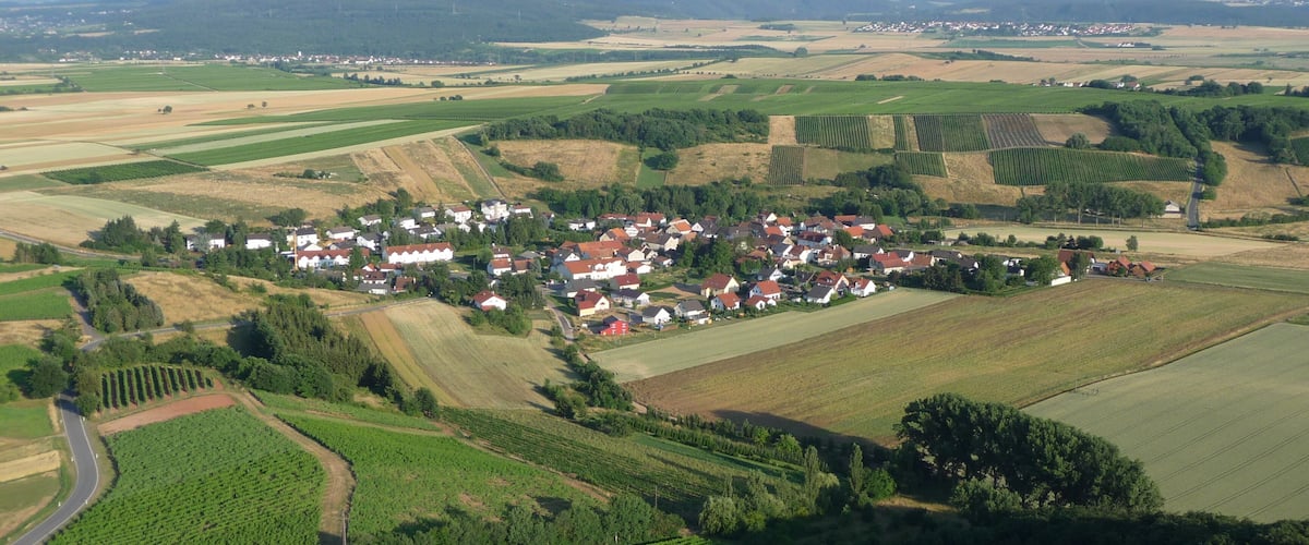 A rural landscape with a small village surrounded by fields and a wind turbine in the distance.