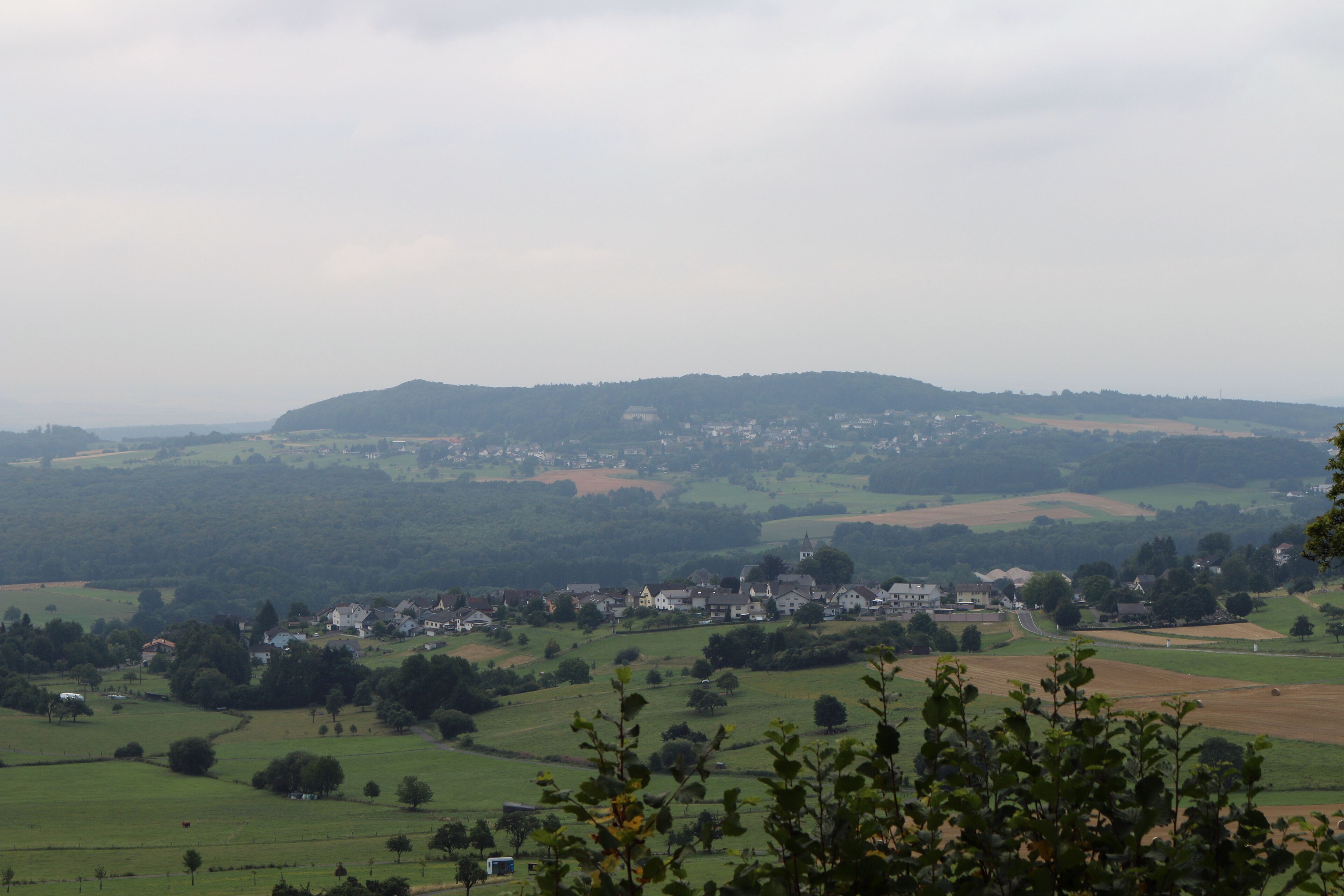 A rural landscape with rolling hills, scattered houses, and a small church.