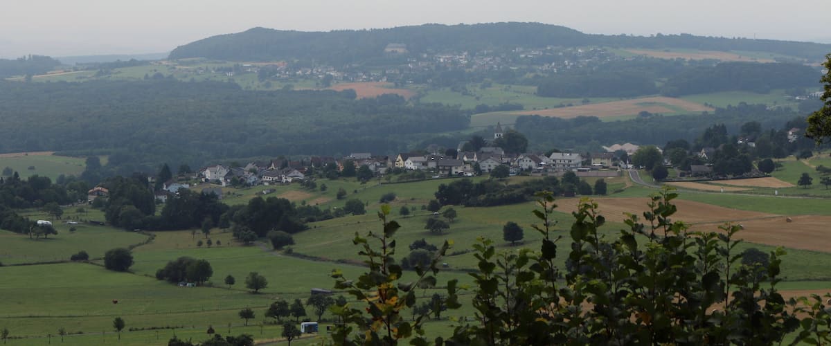 A rural landscape with rolling hills, scattered houses, and a small church.