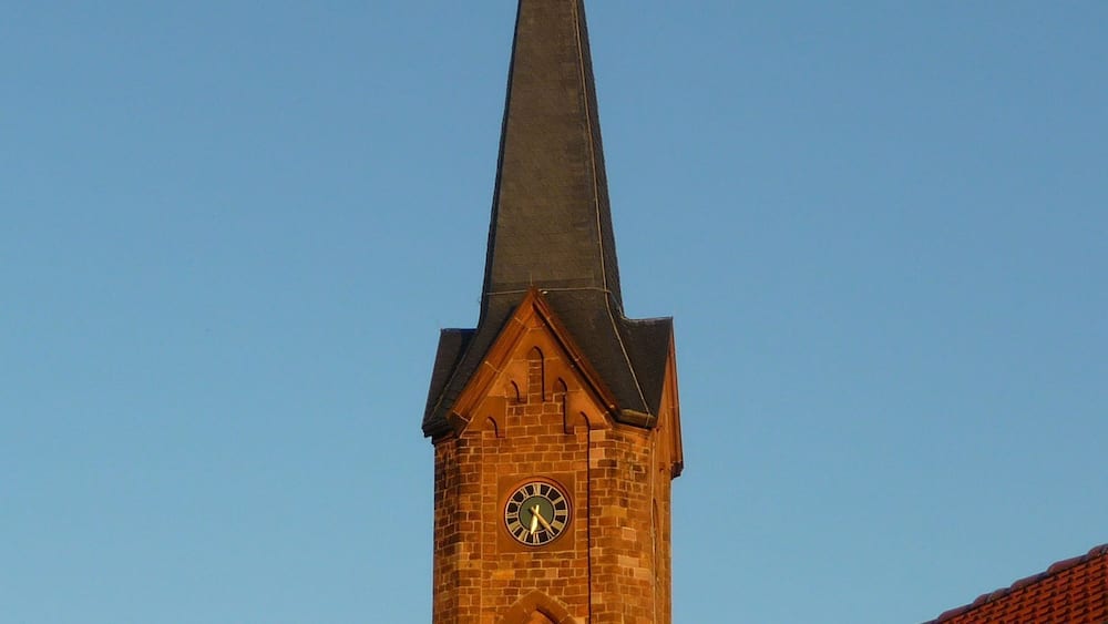 A church tower with a clock and a cross on top.