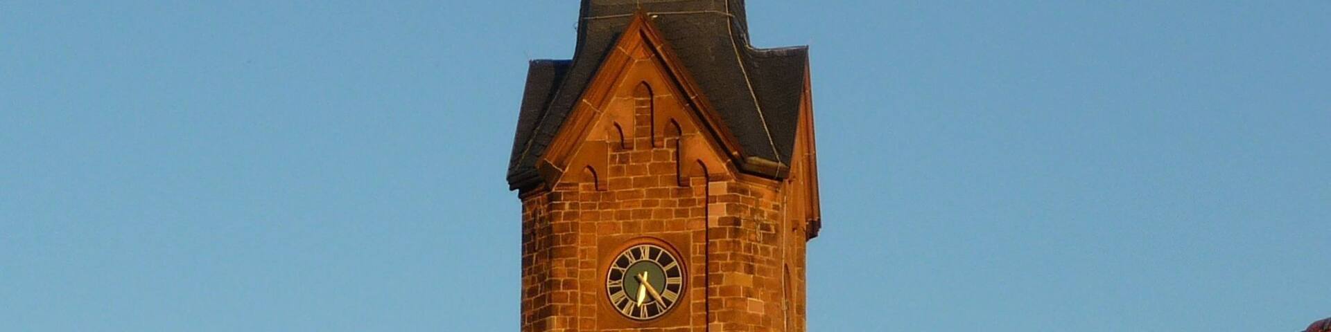 A church tower with a clock and a cross on top.