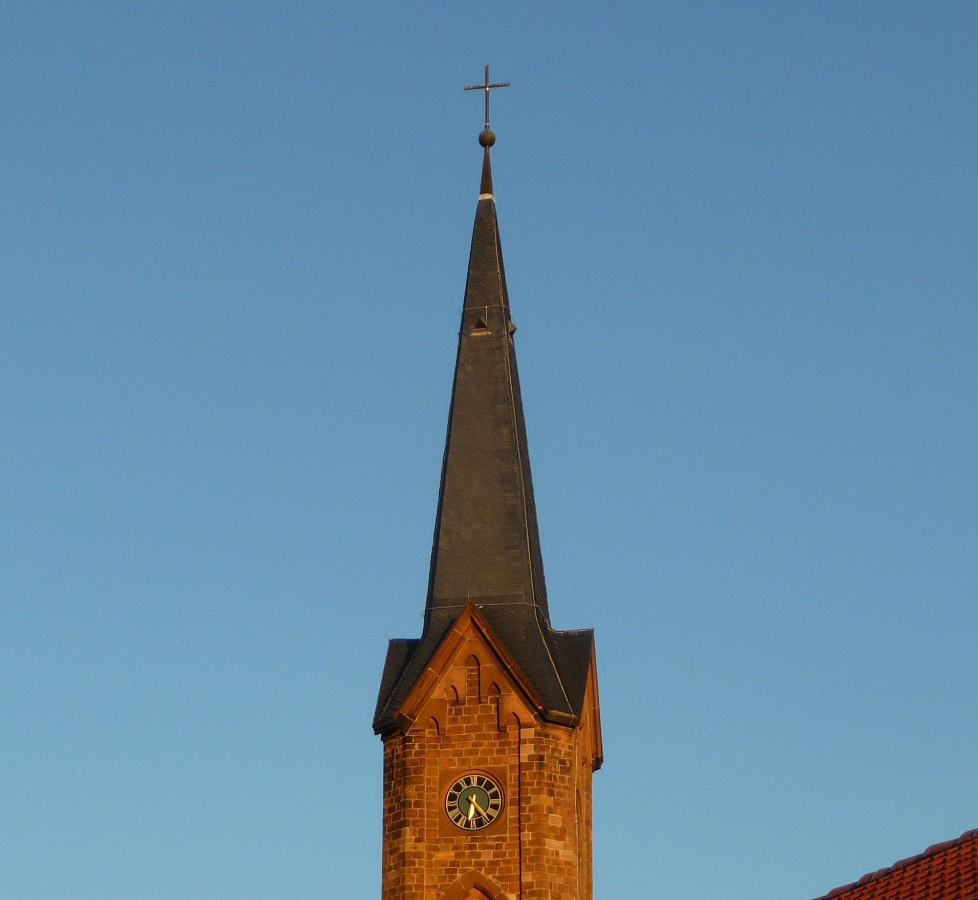 A church tower with a clock and a cross on top.