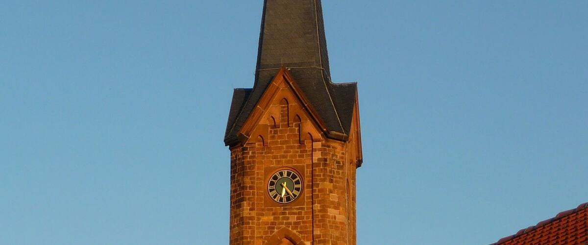 A church tower with a clock and a cross on top.