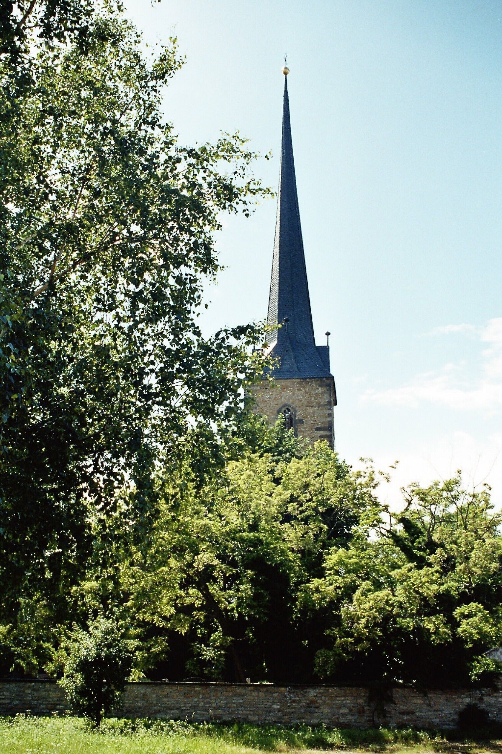 A church with a tall spire, surrounded by trees and a stone wall.