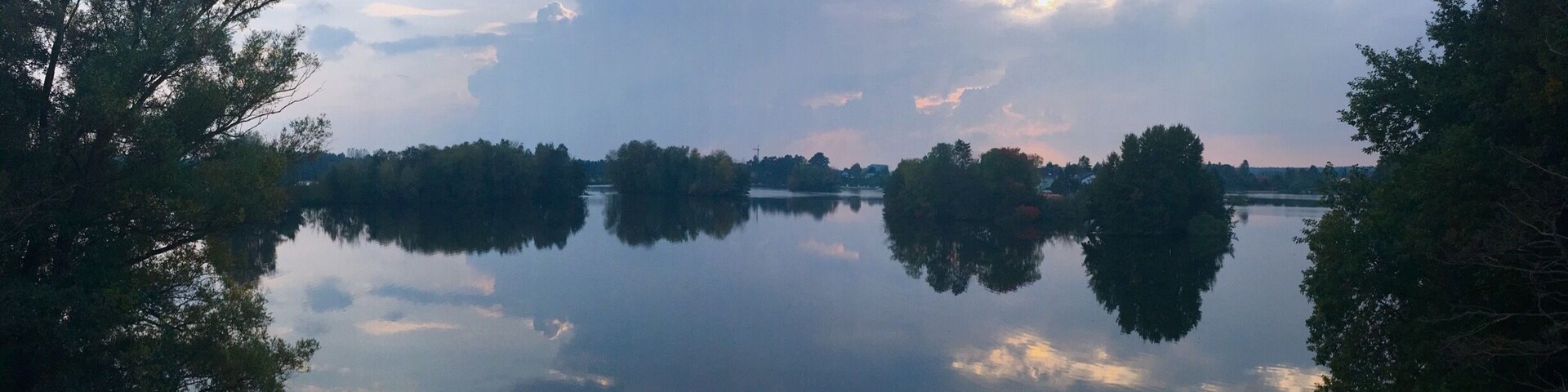 A calm lake with reflections of trees and clouds.