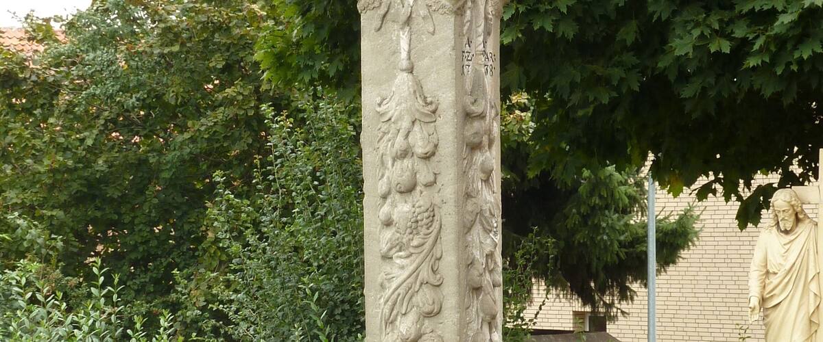 A stone monument with intricate carvings, including a figure holding a book and another figure with a staff, surrounded by lush greenery.