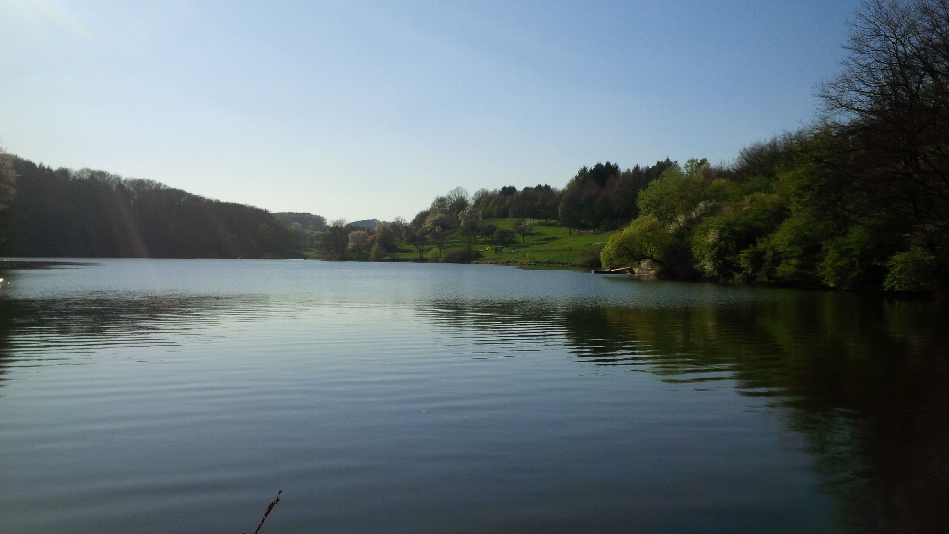 A calm lake surrounded by green hills and trees.