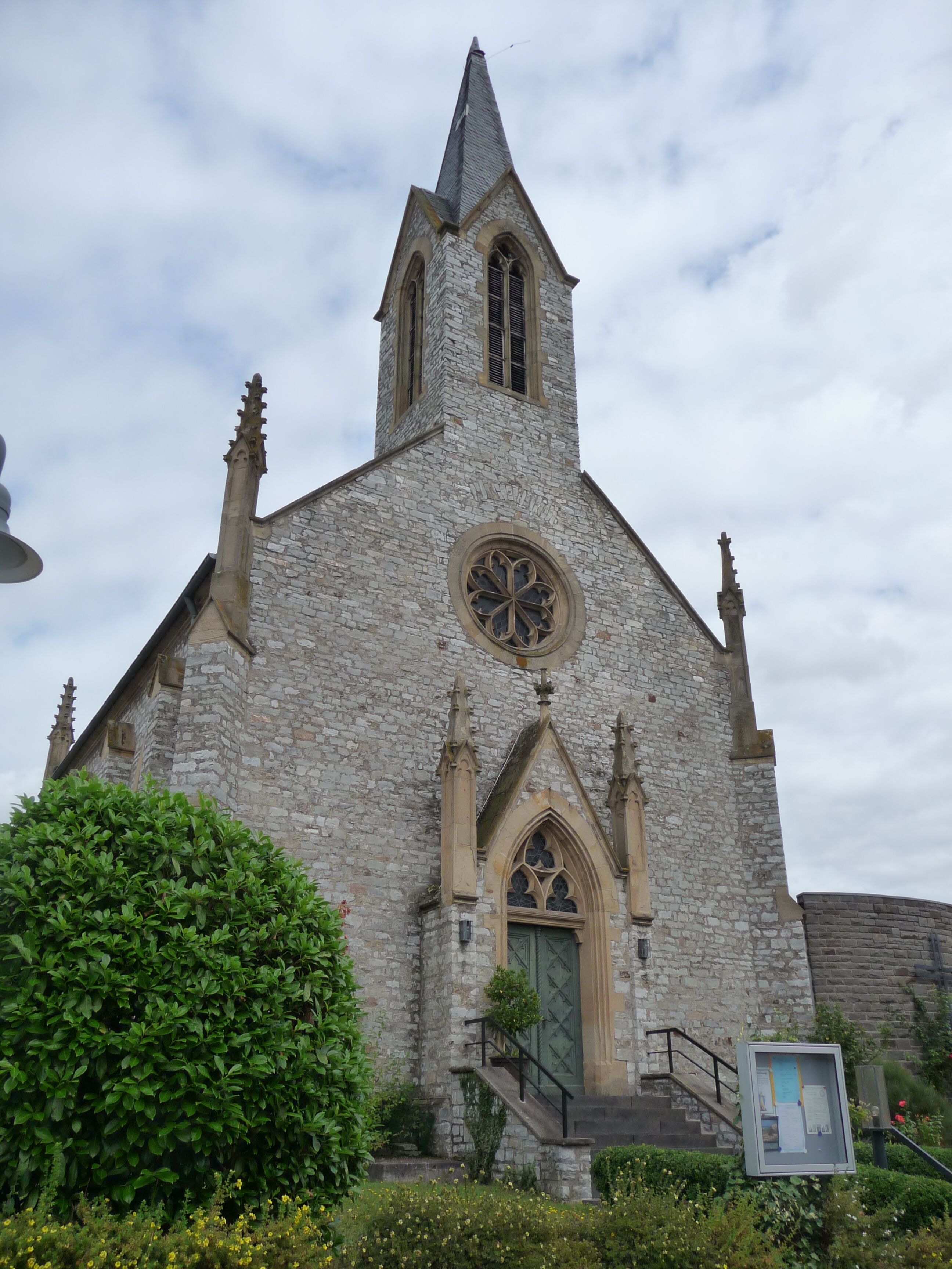 A stone church with a pointed steeple and a circular window.