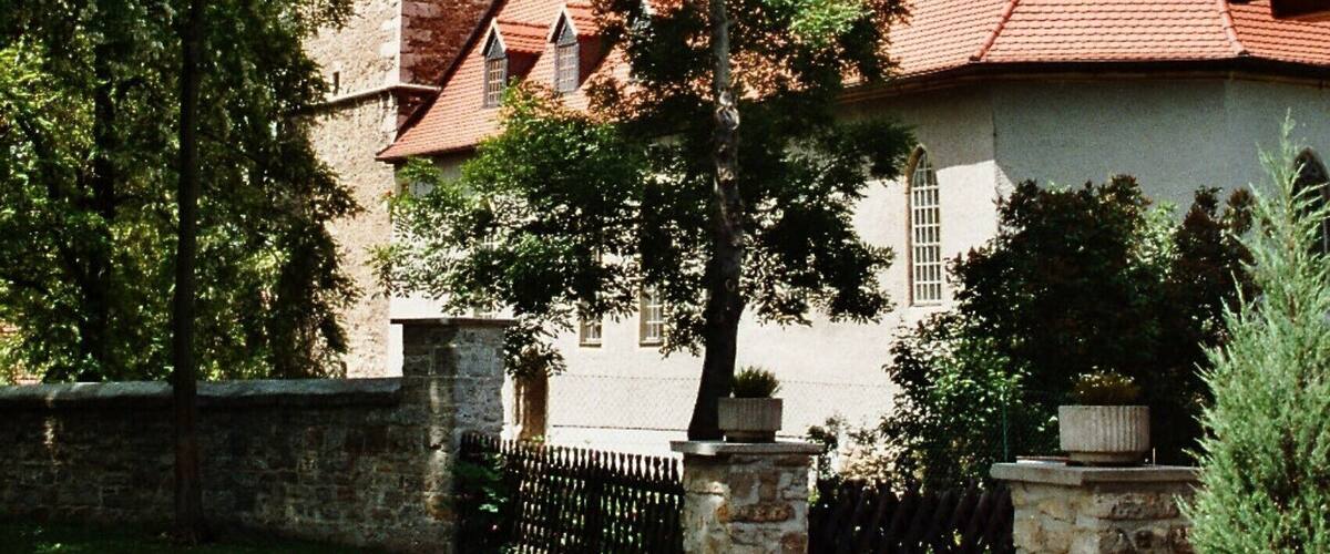 A church with a tall steeple, surrounded by trees and a stone wall.