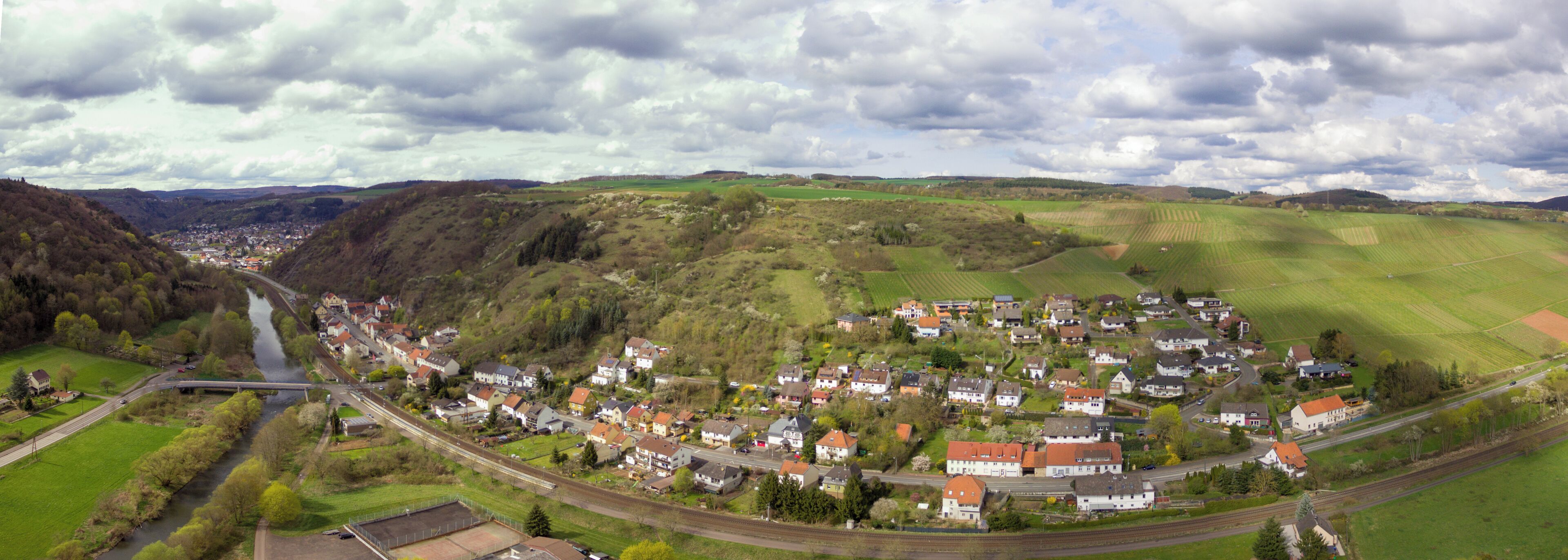 A town nestled in a valley with a river running through it, surrounded by rolling hills and fields.