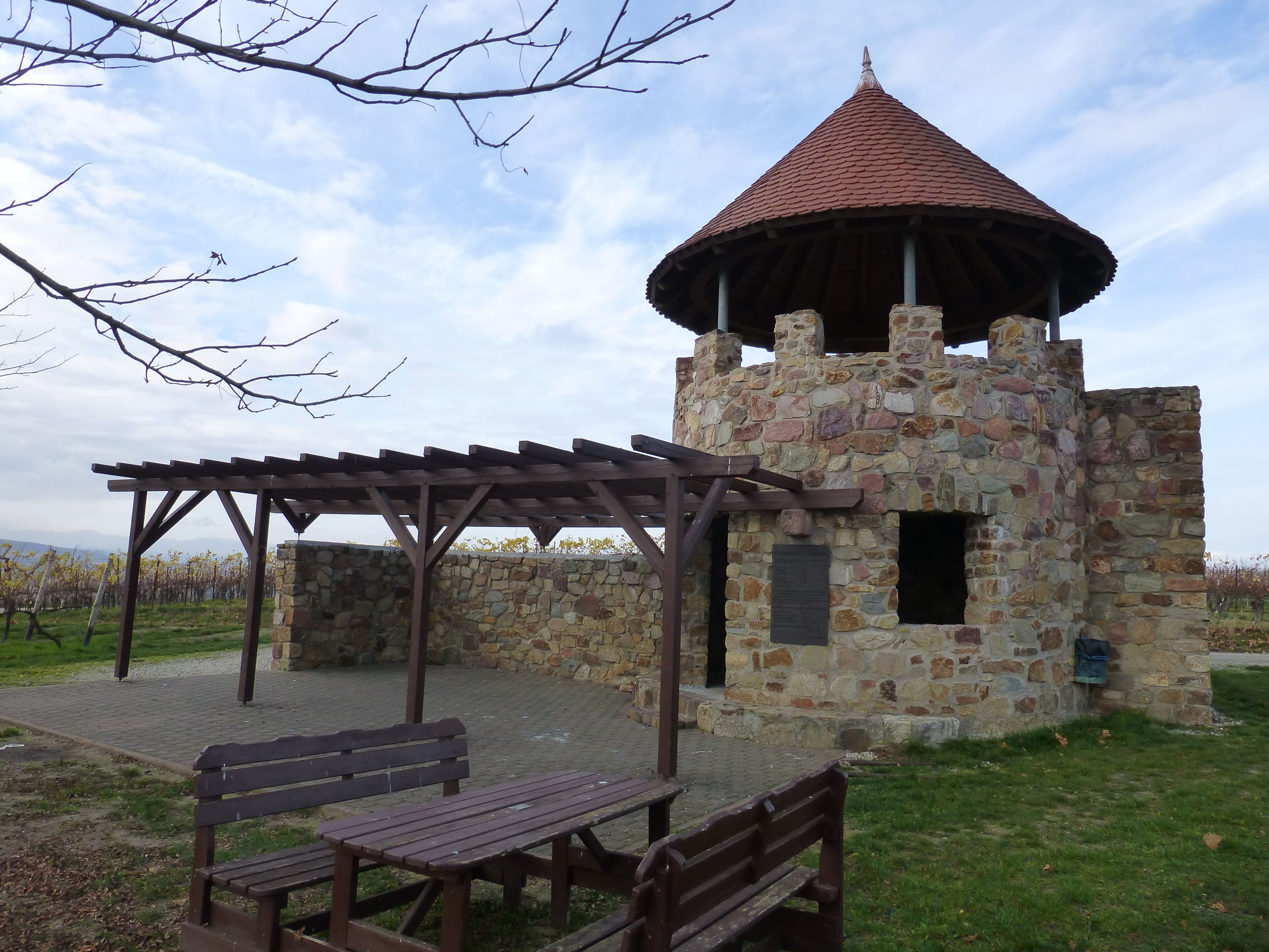 A stone tower with a conical roof, a wooden pergola, and a bench.