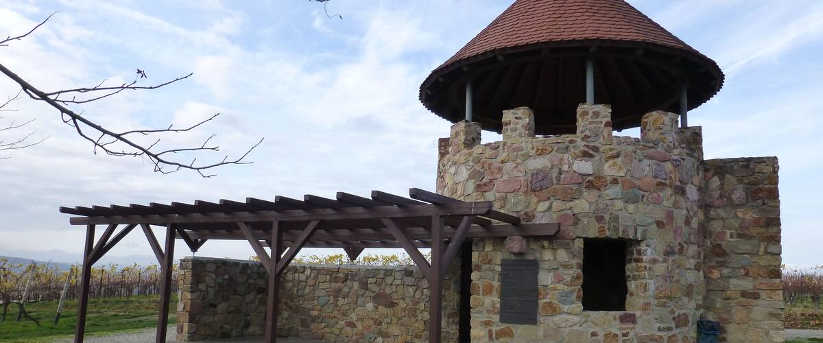 A stone tower with a conical roof, a wooden pergola, and a bench.