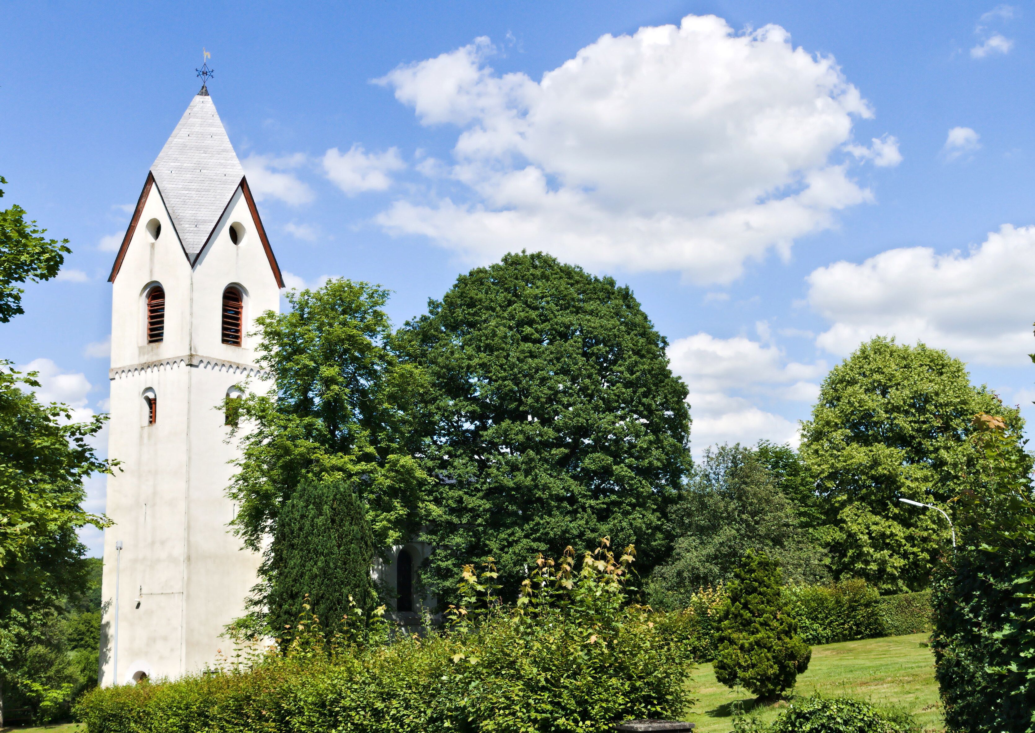 A church with a tall bell tower, surrounded by lush greenery and trees.