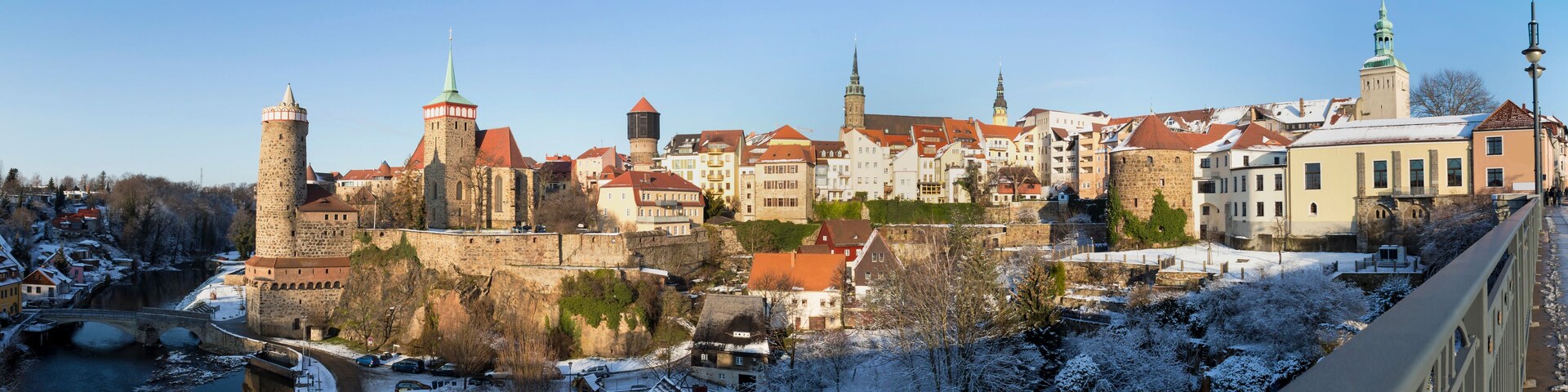 Un pueblo histórico con arquitectura medieval, incluyendo torres y un castillo, rodeado de árboles y edificios cubiertos de nieve.