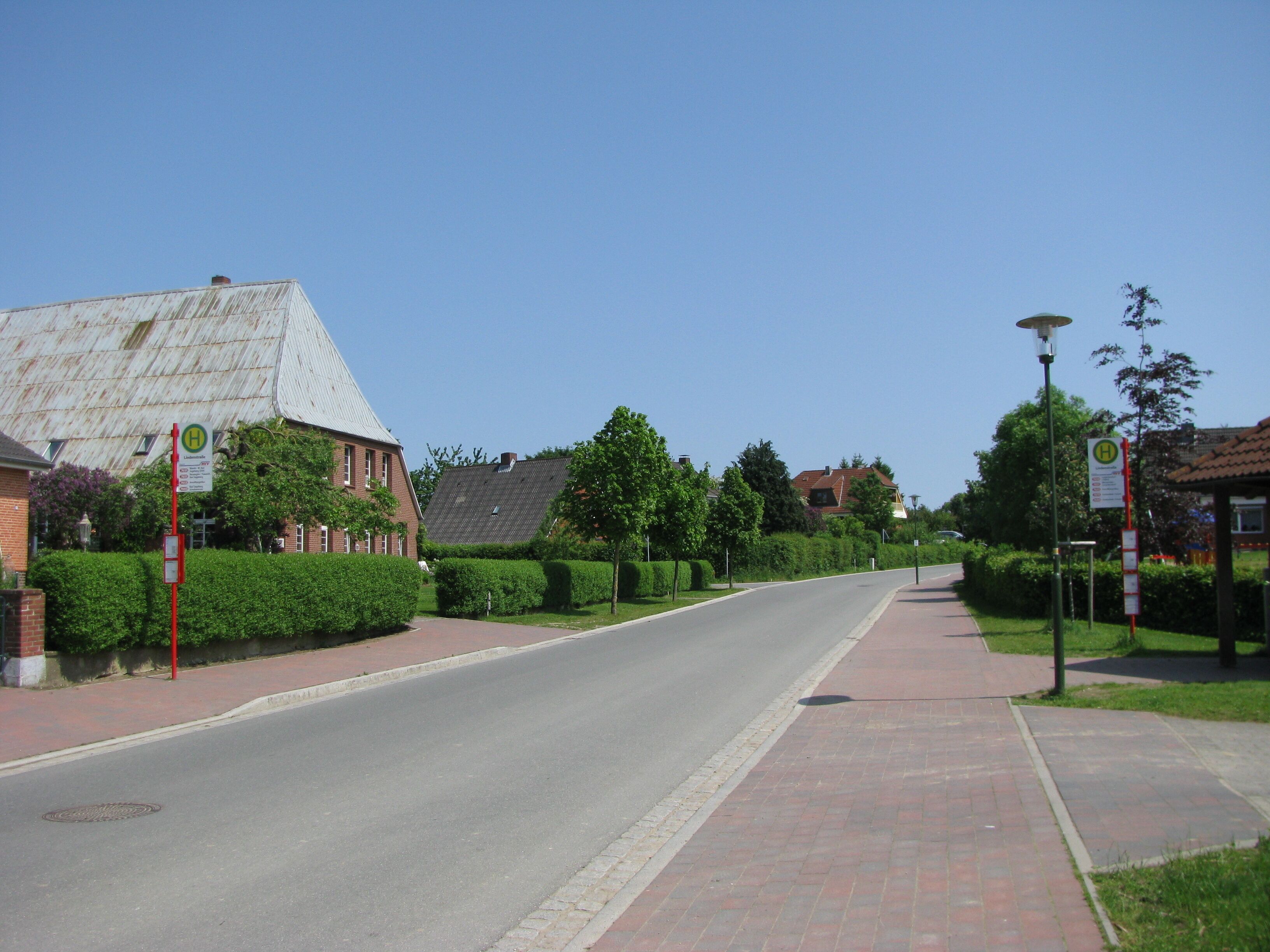 A quiet suburban street with houses, a sidewalk, and street signs.