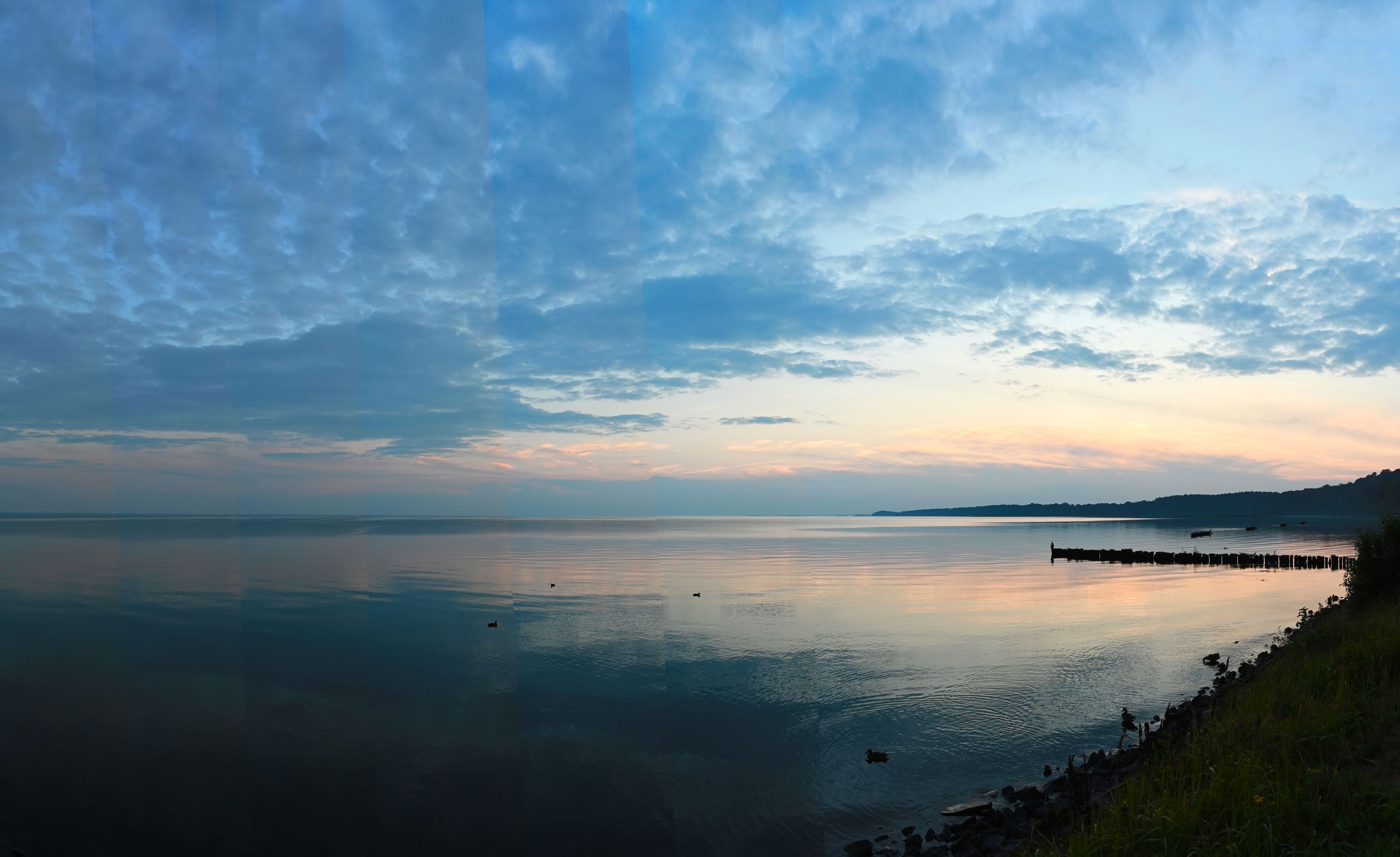 Un lago tranquillo con un molo che si estende nell'acqua, circondato da un paesaggio collinare.