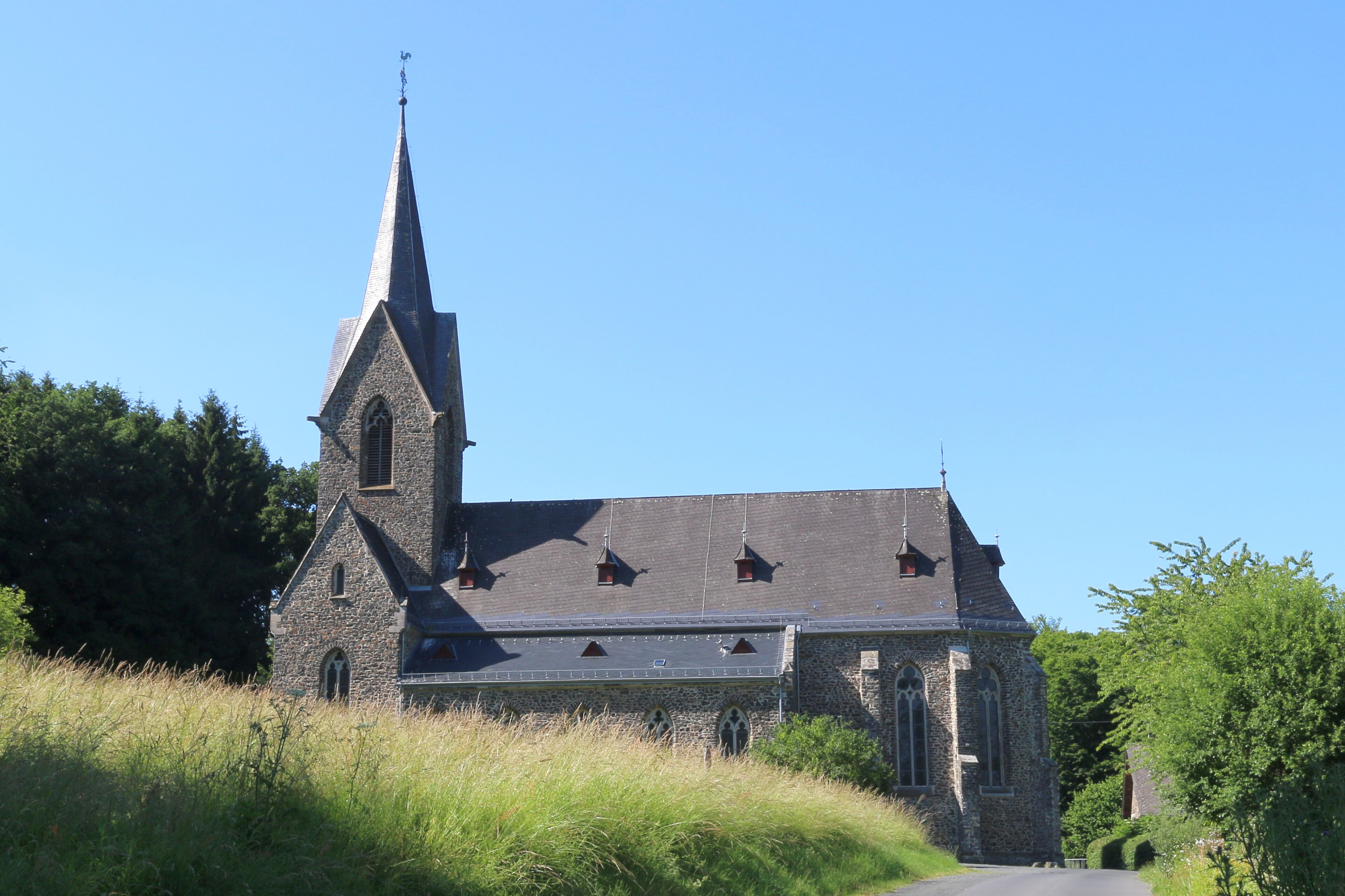 A stone church with a tall steeple and a sloped roof.