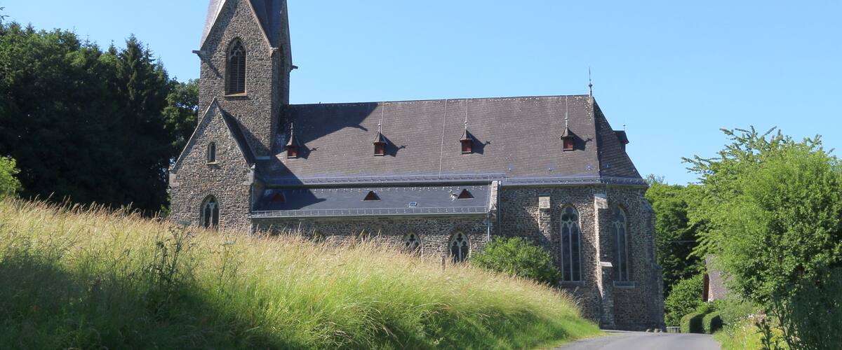A stone church with a tall steeple and a sloped roof.