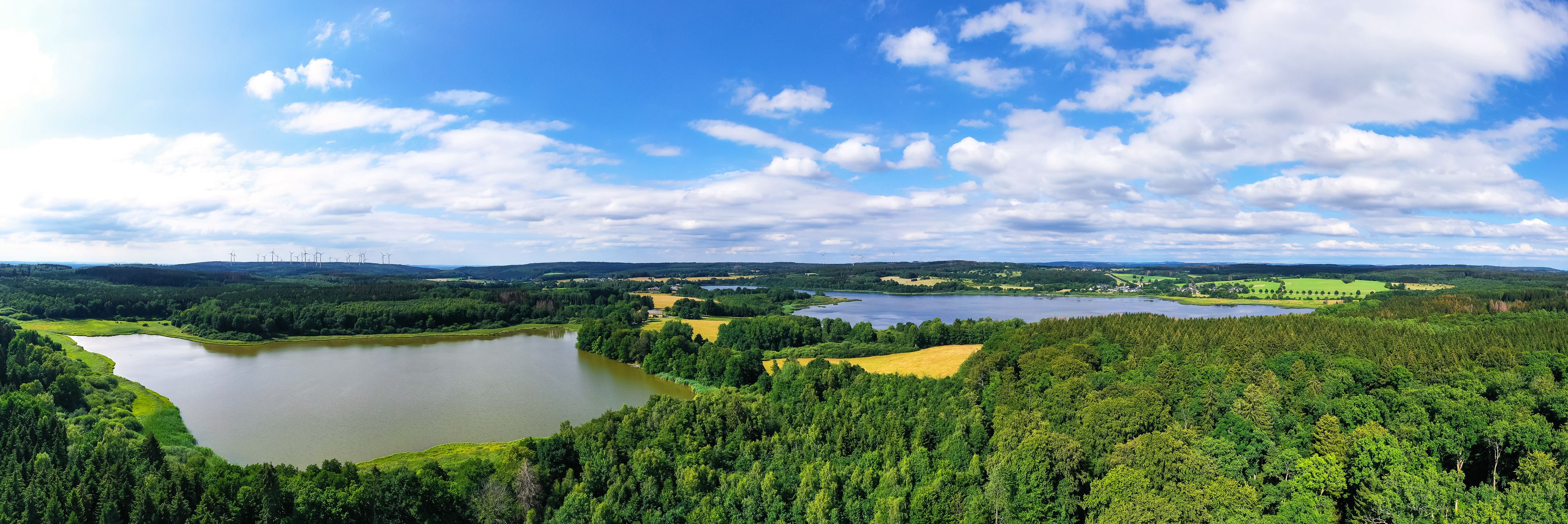 A lake surrounded by dense forests and a clear sky with scattered clouds.