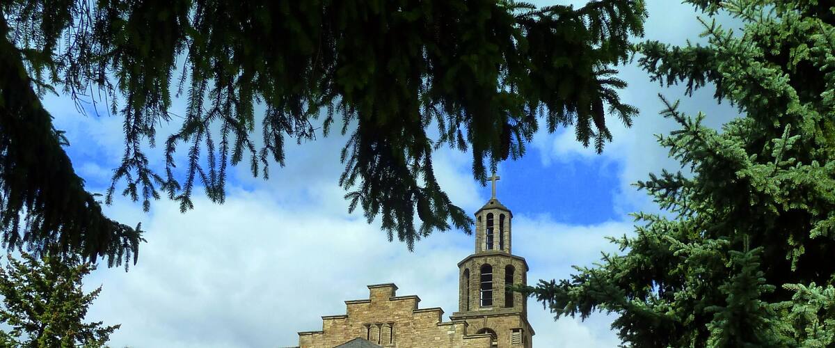 A historic church with a bell tower, surrounded by lush greenery and a clear sky.