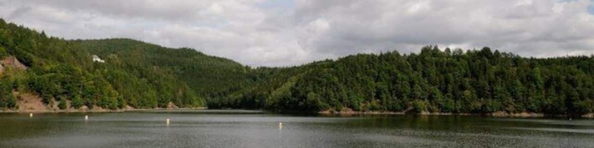 Un lac paisible, entouré de collines boisées, sous un ciel partiellement nuageux.