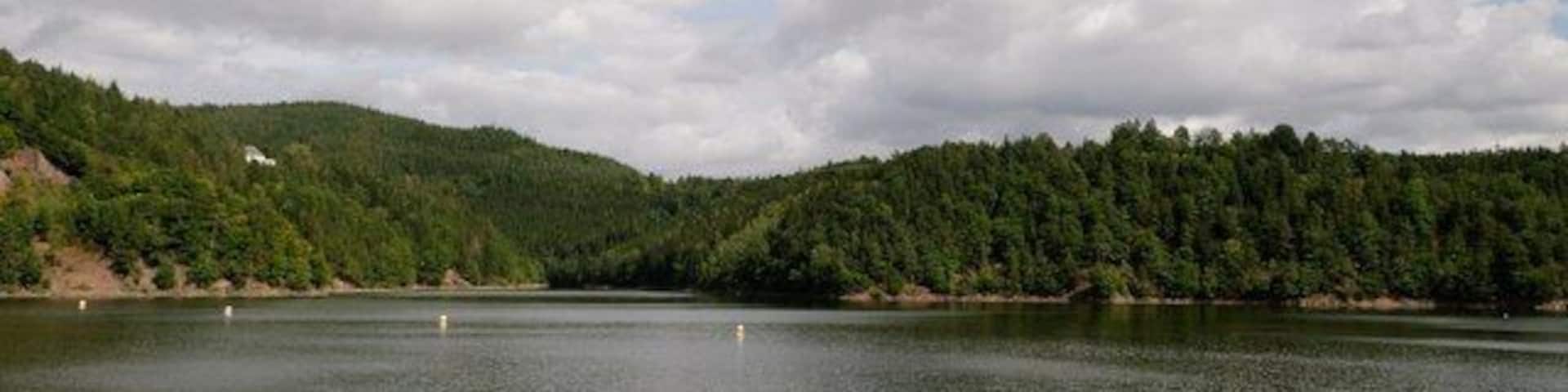A calm lake surrounded by forested hills under a partly cloudy sky.