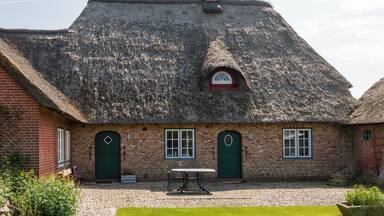 A thatched-roof cottage with a brick exterior, a small garden, and a gravel driveway.