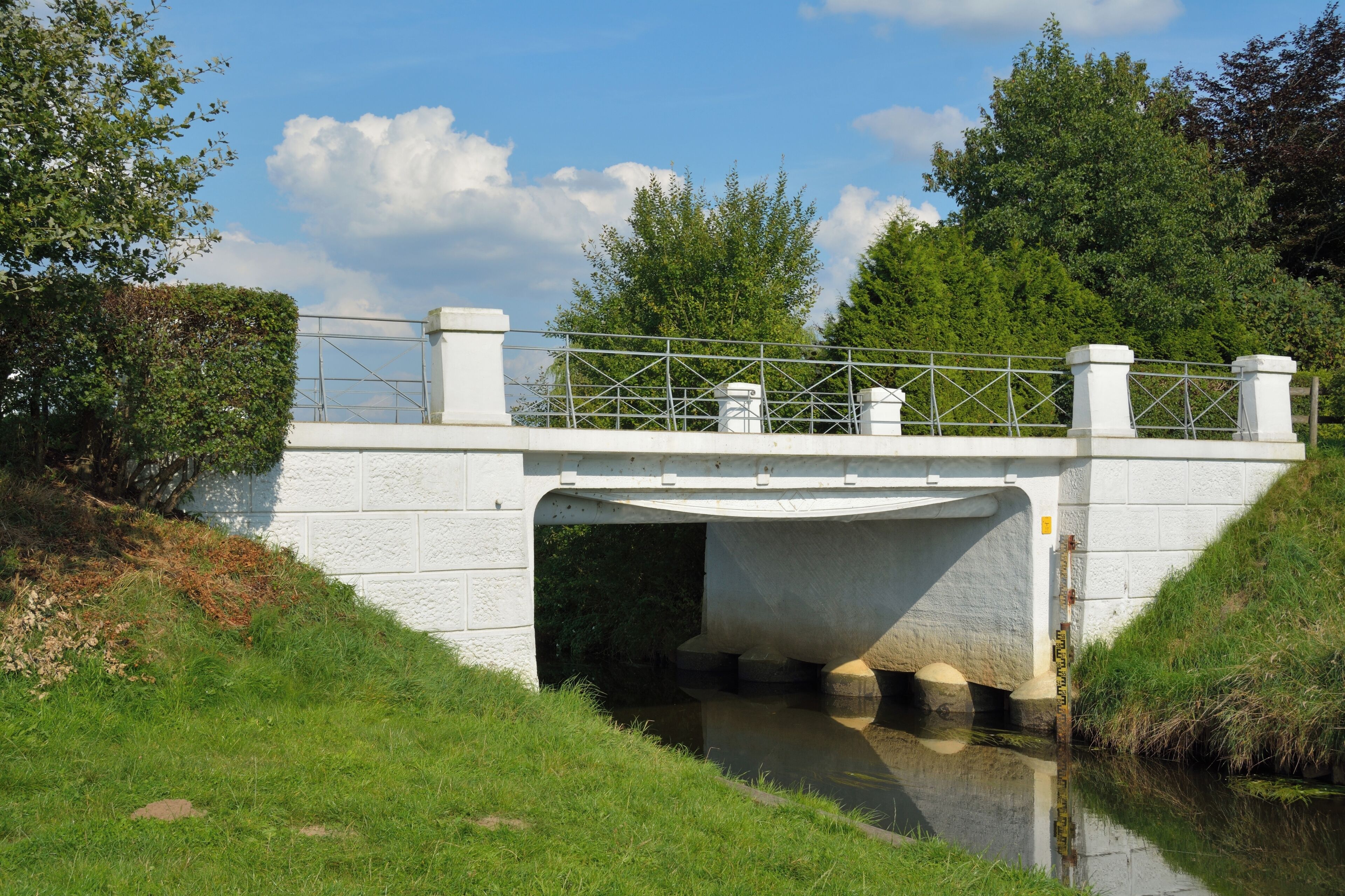 A concrete bridge over a calm waterway, surrounded by lush greenery and trees.