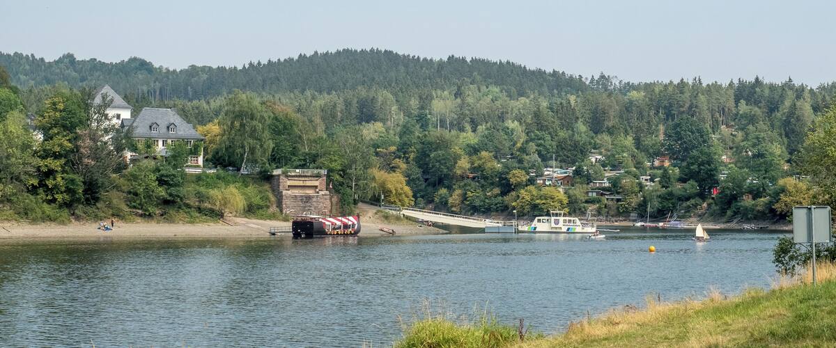 A calm lake with a bridge connecting two land masses, surrounded by dense forest and a few houses.