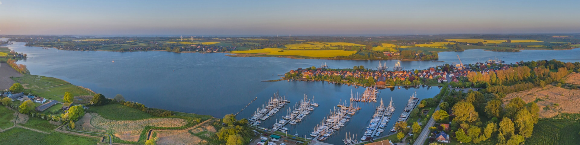 An aerial view of a harbor with numerous boats, a river, and surrounding fields.