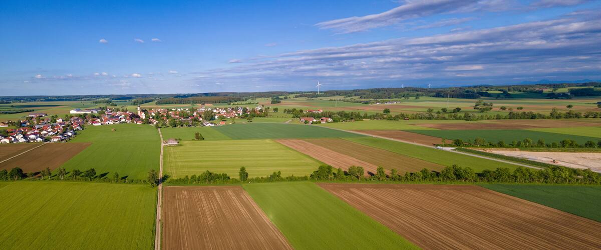 An aerial view of a rural landscape with fields, a small village, and wind turbines.