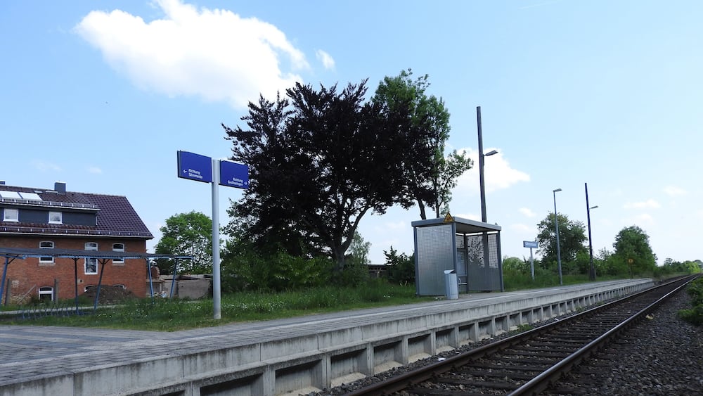 Ein Bahnsteig mit Gleisen, einer Schutzhütte und Hinweisschildern.