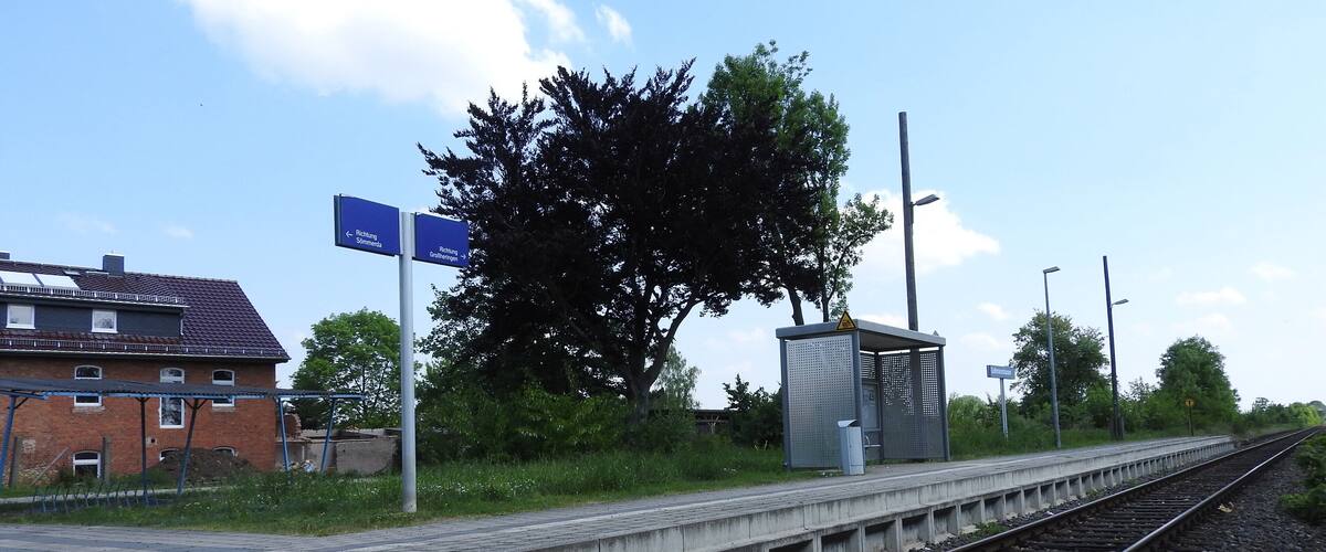 A railway station platform with tracks, a shelter, and directional signs.