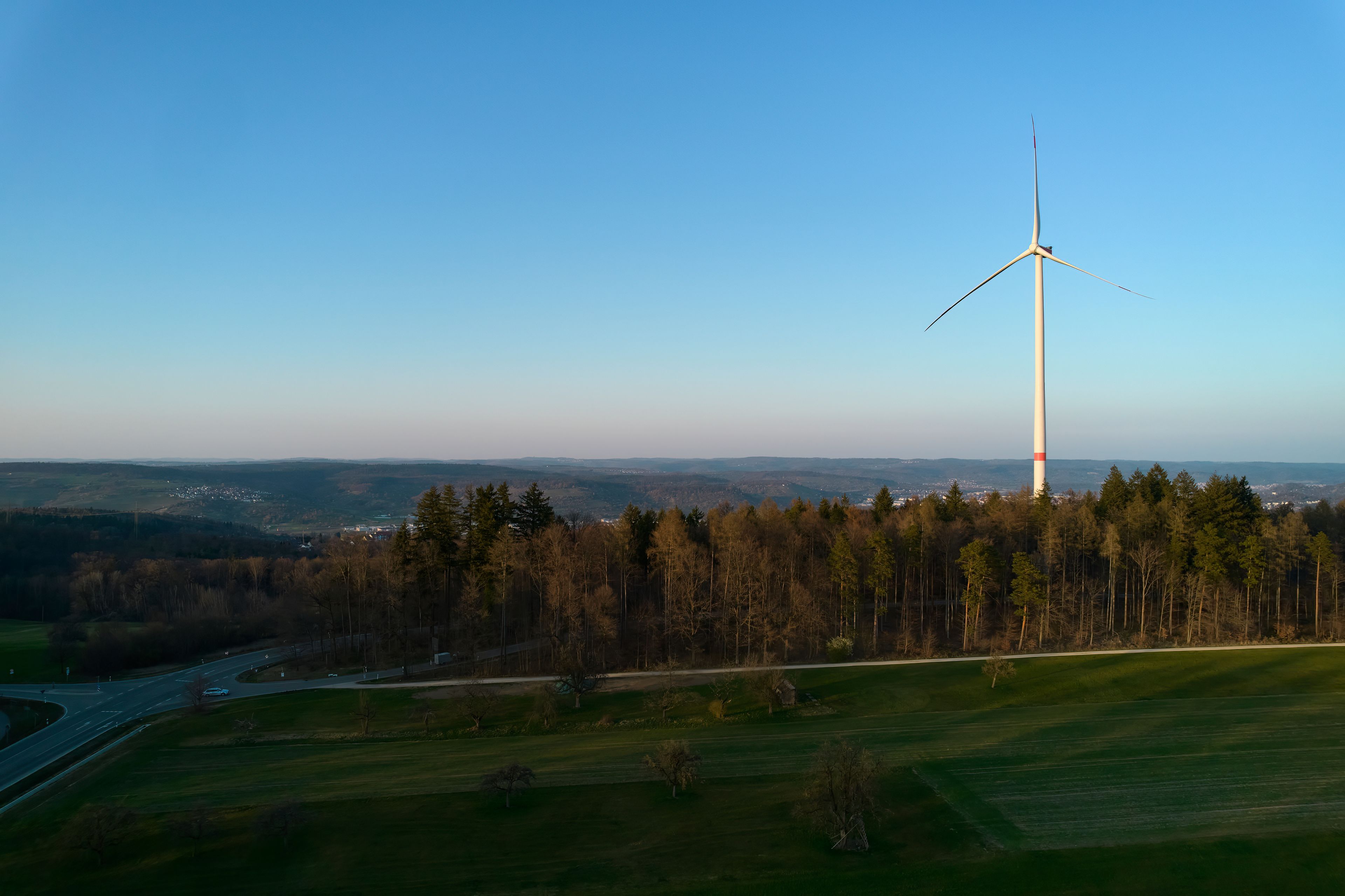 A wind turbine in a forested area with a clear sky.