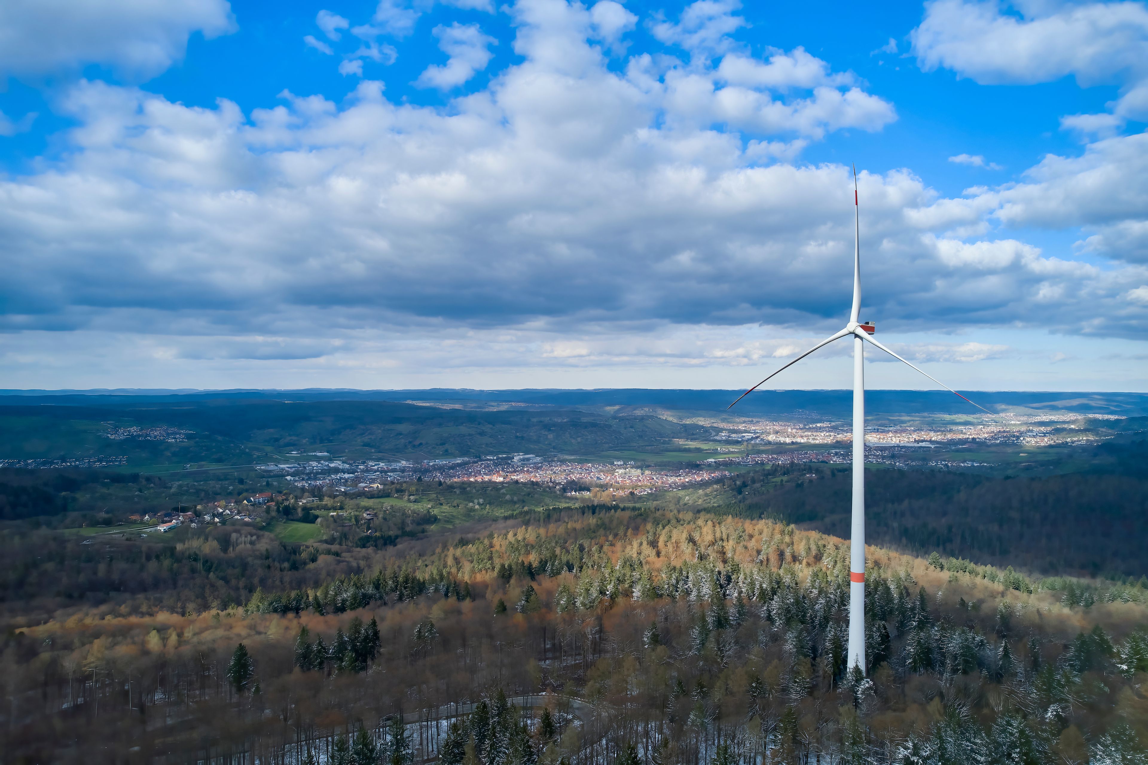A wind turbine in a hilly landscape with a town in the distance.