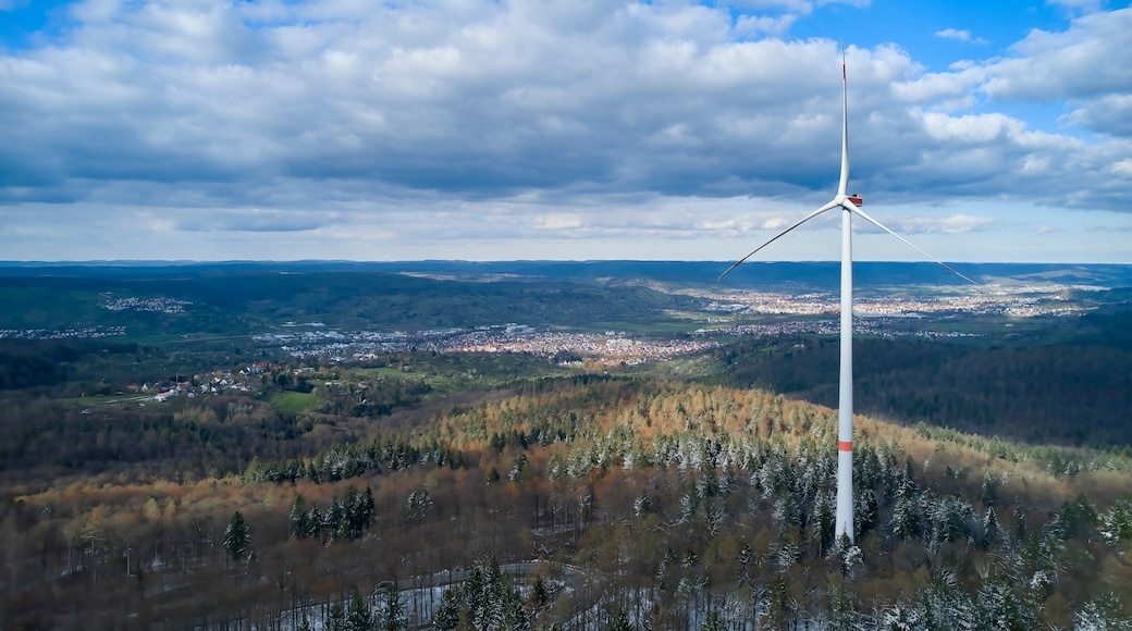 A wind turbine in a hilly landscape with a town in the distance.