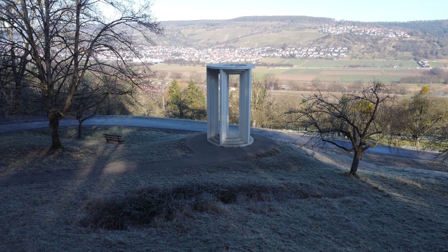 Ein Park mit einer weißen Säulenstruktur, einer Bank und mit Reif bedecktem Gras.