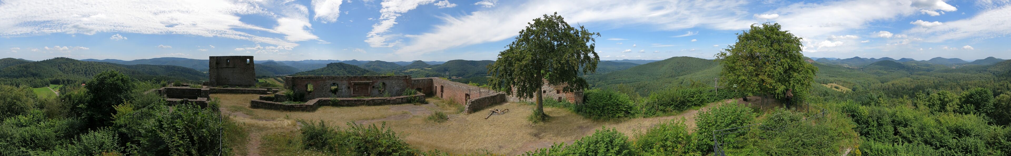 A historical site with ruins and trees in a hilly landscape.