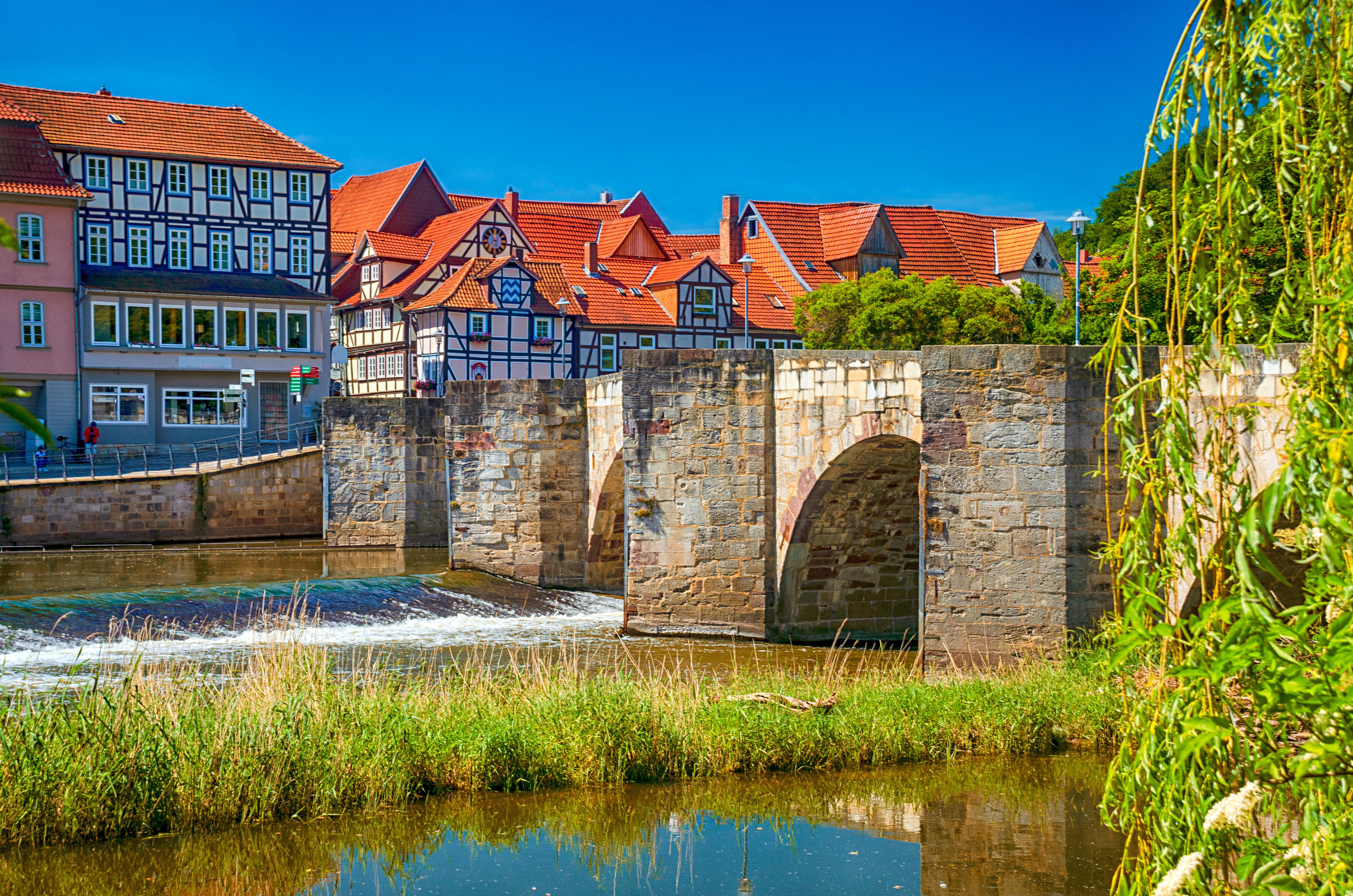 A historic stone bridge over a river, traditional half-timbered houses, and a clear blue sky.