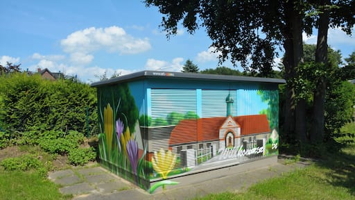 Un cuadro de control lleno de grafitis de colores en un área verde con árboles y cielo despejado.