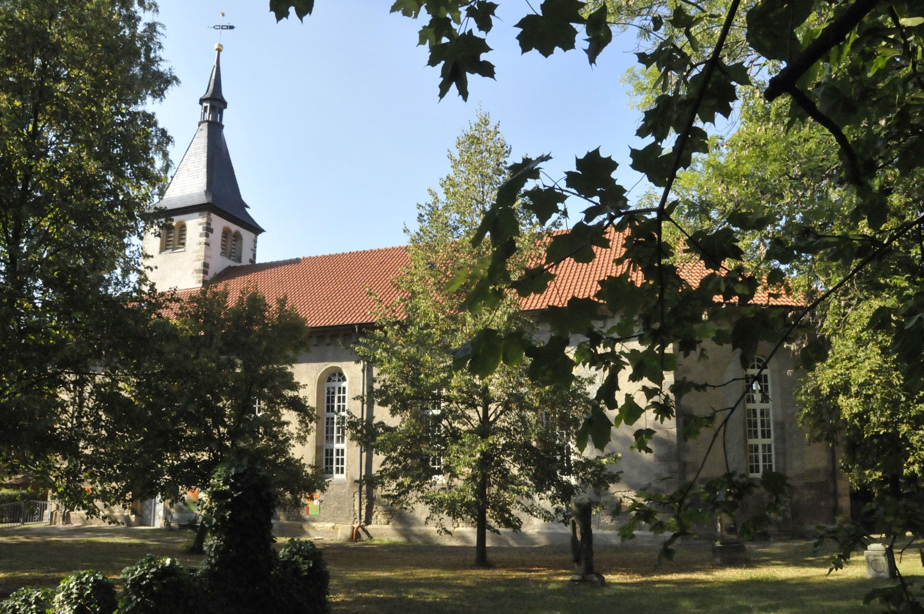 A church with a red-tiled roof and a steeple, surrounded by trees and a well-maintained lawn.