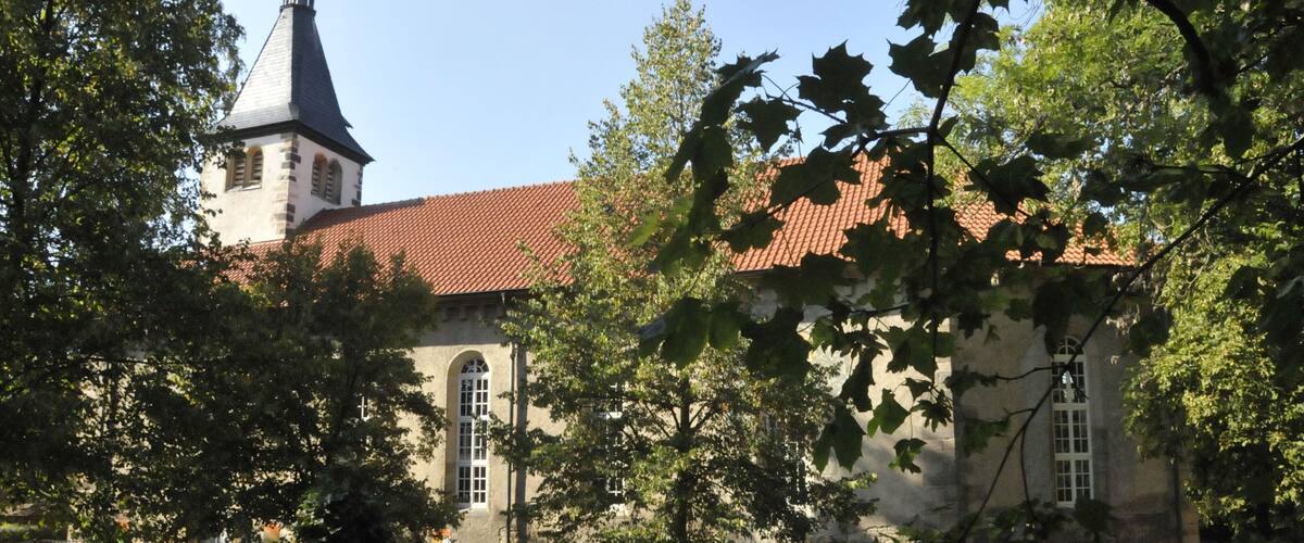 A church with a red-tiled roof and a steeple, surrounded by trees and a well-maintained lawn.