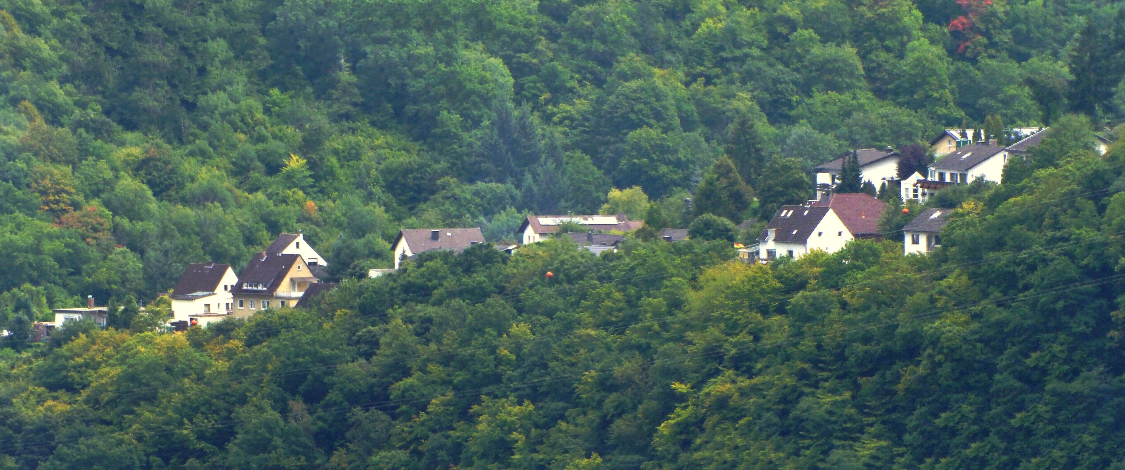 A hillside village with houses nestled among dense green trees.