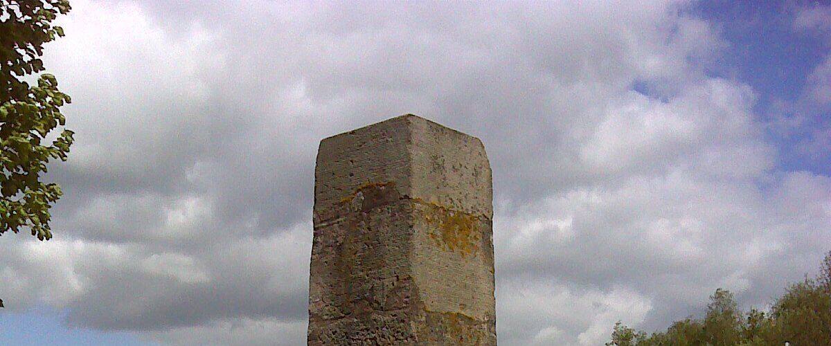 A tall stone monument with inscriptions, surrounded by grass and a road with a traffic island.